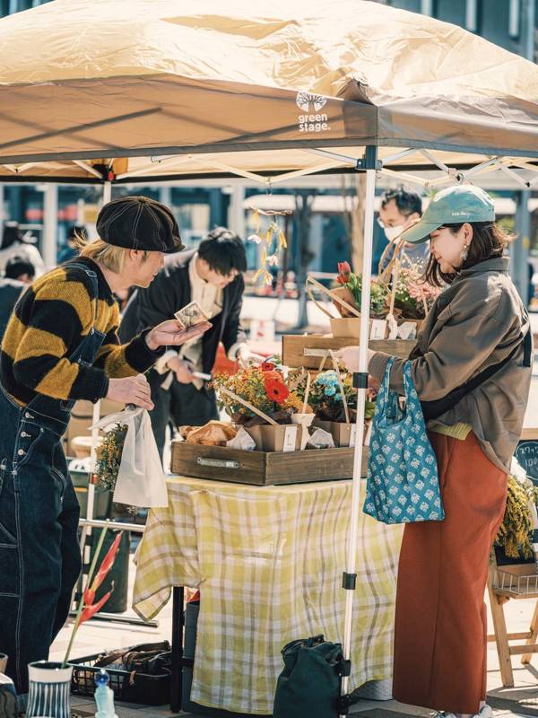テントの下で店主と来場者が品物を見ながら話している